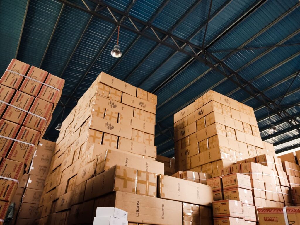 heros-img High stacks of cardboard boxes organized in a warehouse with a blue metal ceiling.